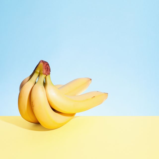 still life shot of bunch of five bananas on yellow table with blue background