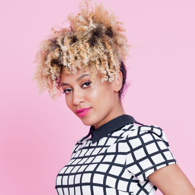 summer portrait of beautiful afro american young woman standing with hand is pocket, against pink wall wearing grid check playsuit, studio shoot