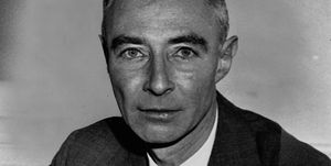 j robert oppenheimer looks at the camera with a neutral expression on his face in a black and white photo, he wears a dark suit with a white collared shirt and dark tie