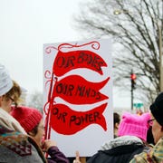 Women's March with Protest Sign crowds of women and men holding protest signs march through the streets during the women's march on washington, dc prominent sign says, "our bodies, our minds, our power" protest march community togetherness