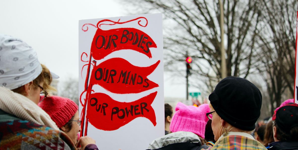 crowds of women and men holding protest signs march through the streets during the women's march on washington, dc prominent sign says, "our bodies, our minds, our power" protest march community togetherness