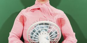Midsection of businesswoman with sweaty armpits holding fan against green background