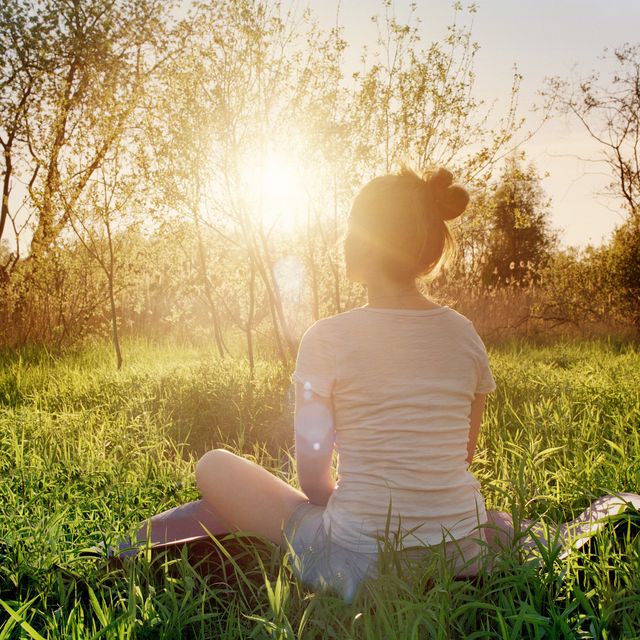 young woman sitting in yoga position enjoying sunset in nature