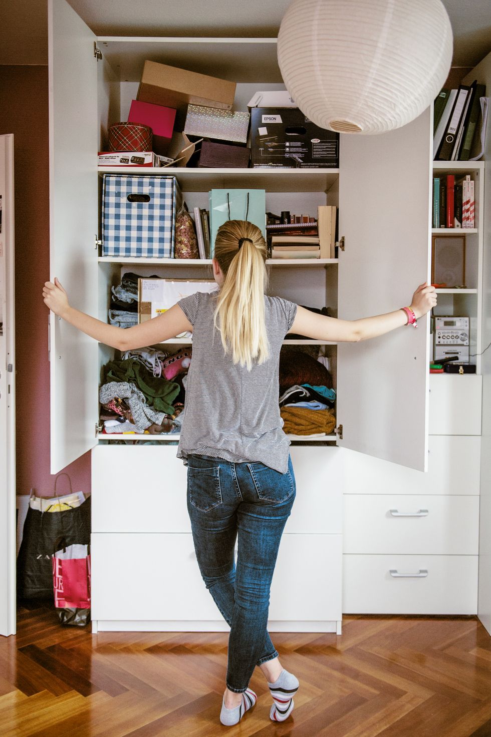 teenage girl with long blonde hair, opening doors of cabinet in her room and inspecting content