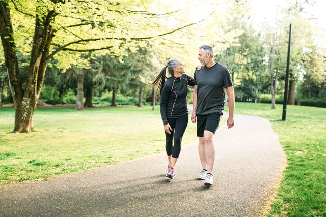 a healthy adult couple in their mid 50s walk in a beautiful park setting, enjoying the exercise and fresh air a depiction of healthy lifestyle choices, relationships, and aging