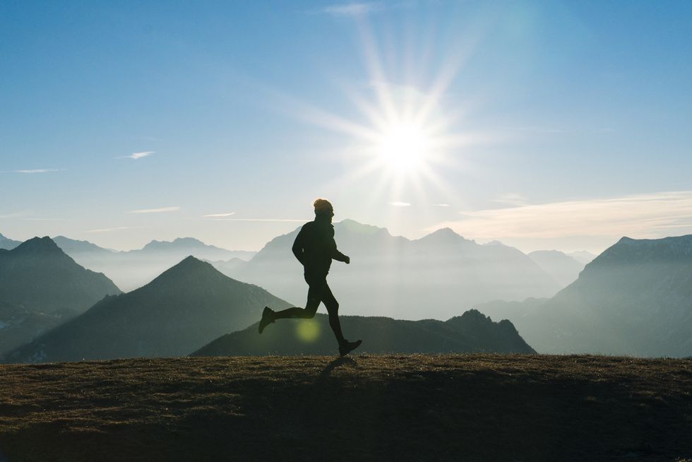 Trail runner strides across mountain summit, sunrise
