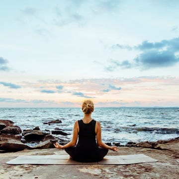 Young woman performs yoga moves on bluff above sea