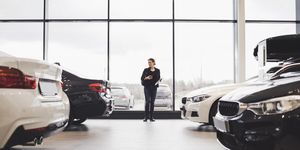 full length of woman standing amidst cars in showroom