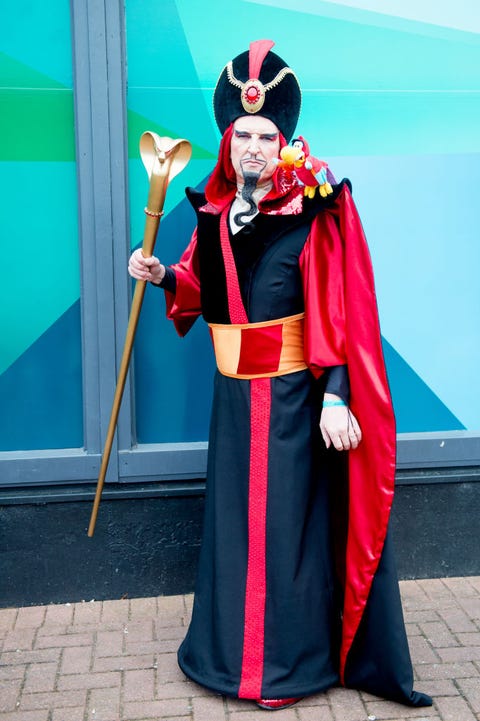 a cosplayer as jafar from aladdin with golden serpent staff and black and red floor length robe on brick road