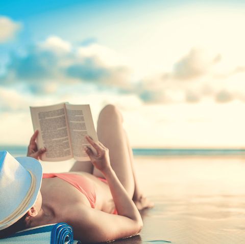 una mujer tumbada en la playa leyendo un libro