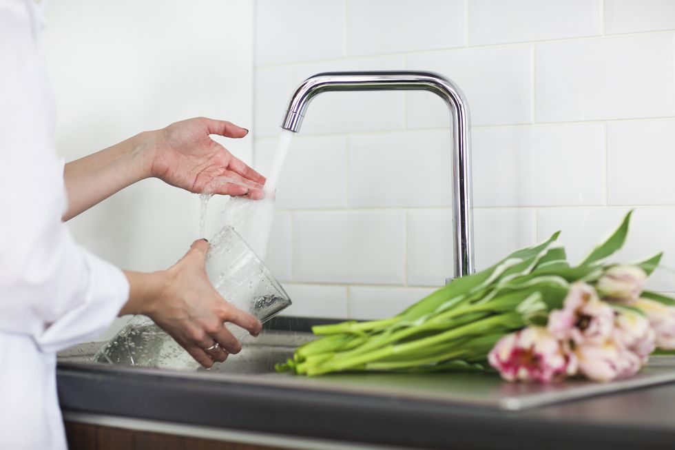young woman rinsing and cutting flowers and pouring water into the vase in kitchen sink close up
