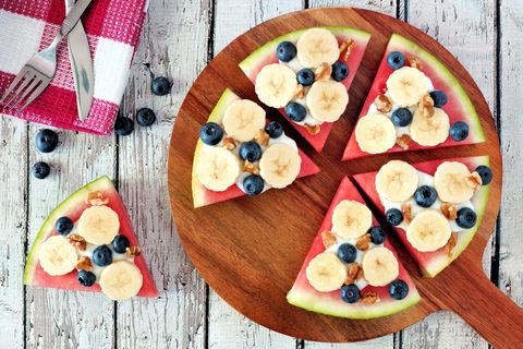 sliced, juicy watermelon pizza with bananas, blueberries, nuts and yogurt, above view on wood serving board