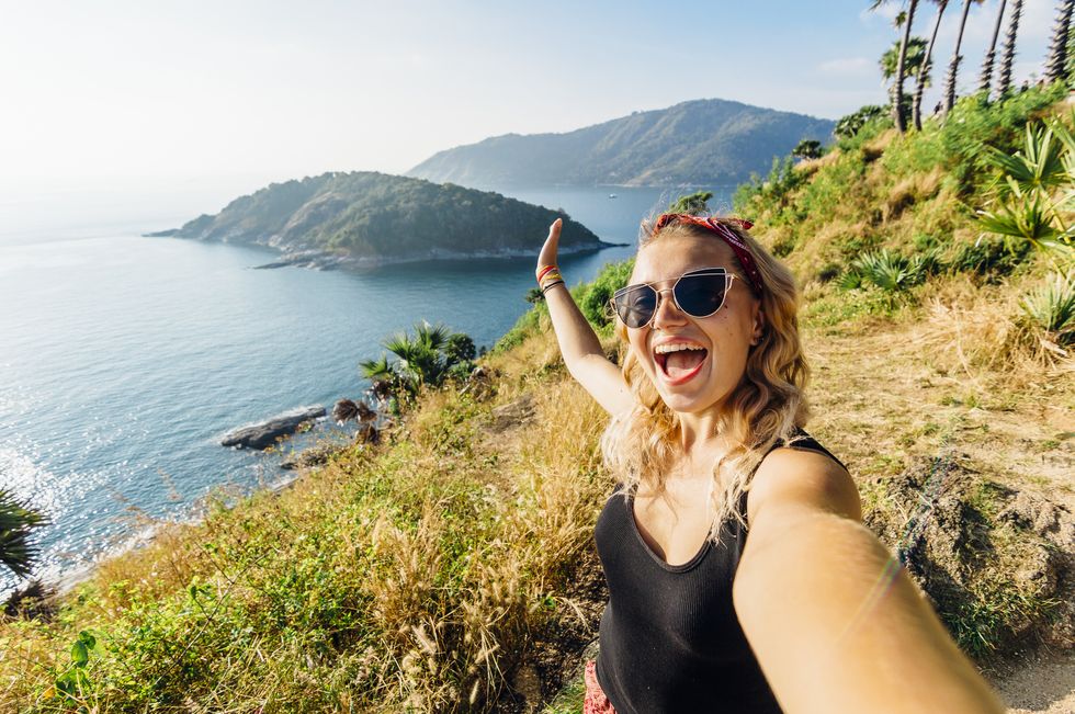 young woman takes selfie, on hillside above sea