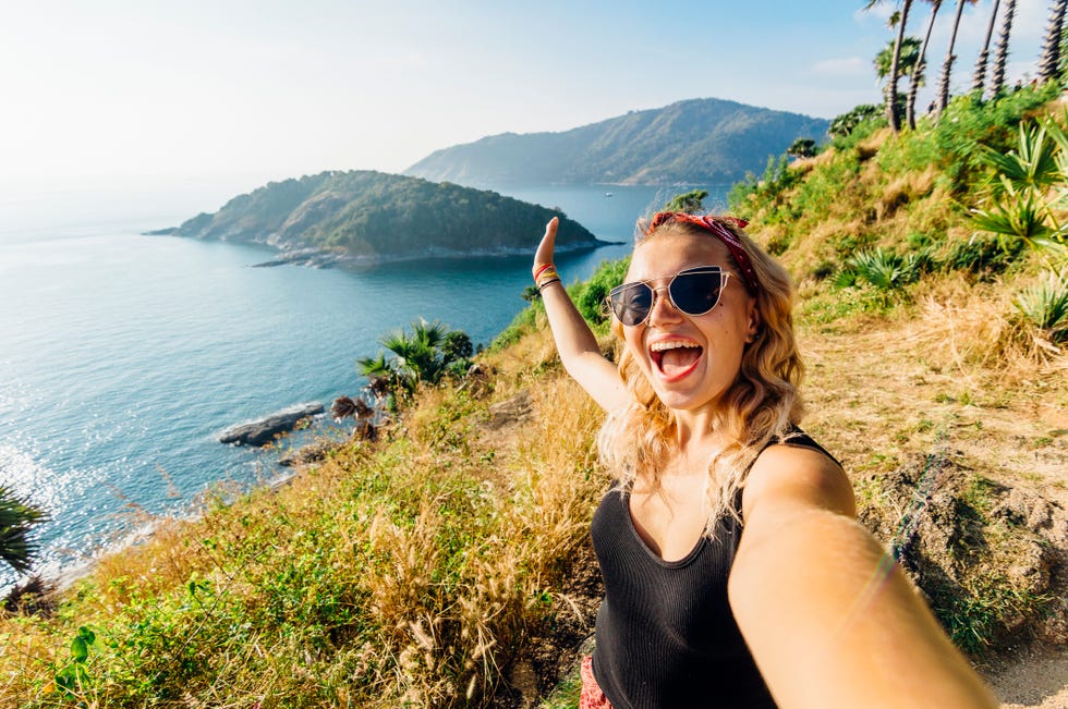 young woman takes selfie, on hillside above sea