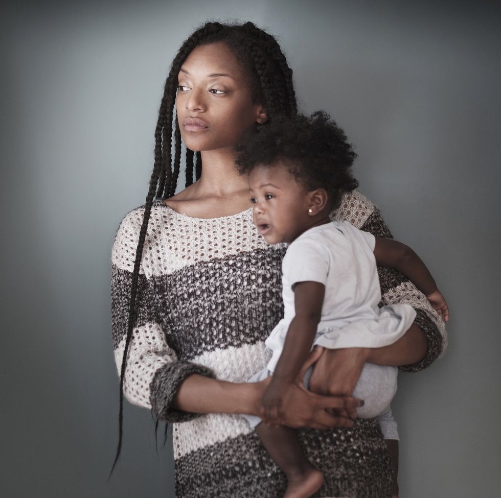 Thoughtful Black woman standing holding baby daughter