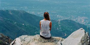Vista de espaldas de una mujer sentada en lo alto de una montaña
