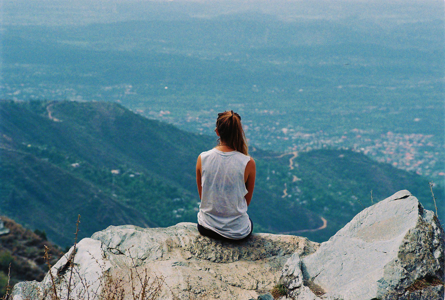 Vista de espaldas de una mujer sentada en lo alto de una montaña