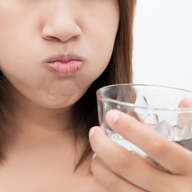 Healthy happy woman rinsing and gargling while using mouthwash from a glass, During daily oral hygiene routine, Portrait with bare shoulders, Dental Health Concepts