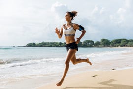 asia, indonesia, bali, woman sprinting along beach, wearing smart phone hoder and listening to earphones