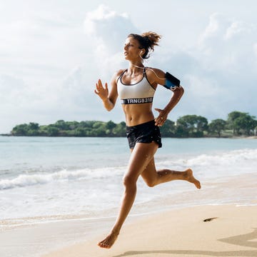 asia, indonesia, bali, woman sprinting along beach, wearing smart phone hoder and listening to earphones