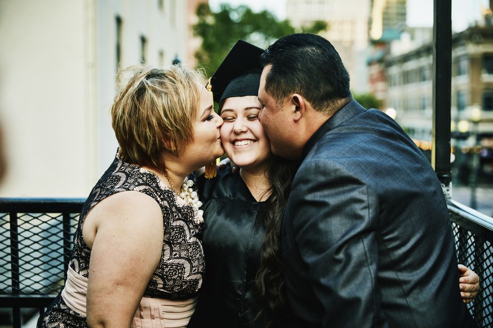 mother and father kissing graduating daughter during family celebration