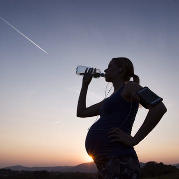 pregnant woman drinking water from bottle at sunset