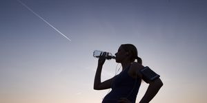 pregnant woman drinking water from bottle at sunset