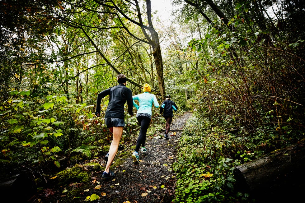 group of female friends running up forest trail on rainy afternoon