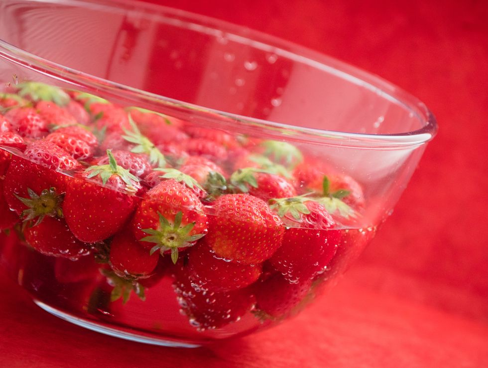 strawberries in water glass bowl reddish background