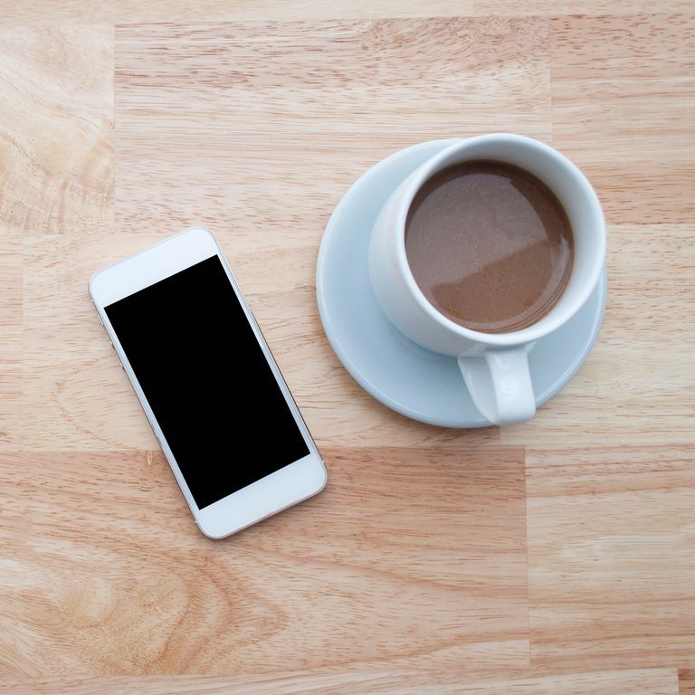 High Angle View Of Fresh Latte Served By Mobile Phone On Table