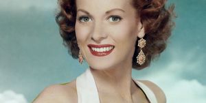 maureen o'hara smiles at the camera, she wears red lipstick, large dangling earrings and a white halter top