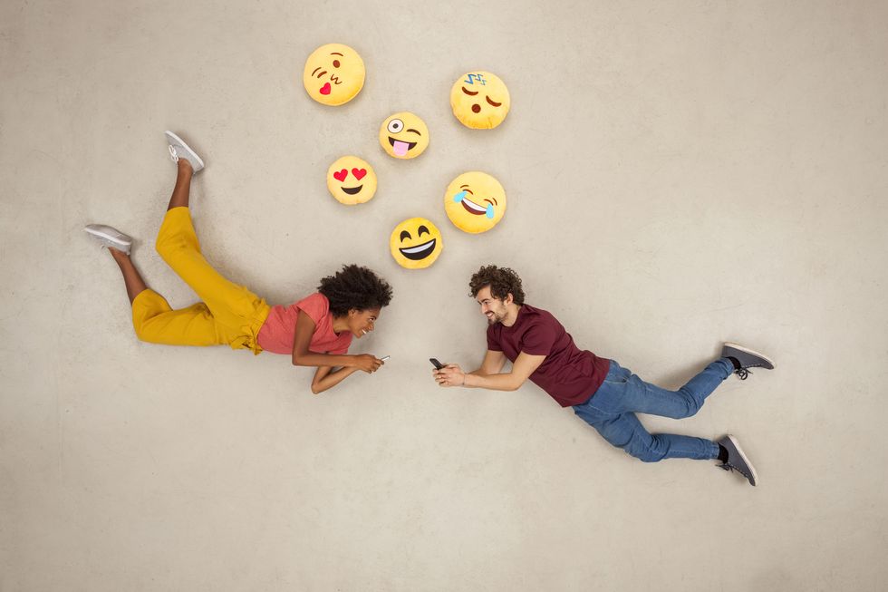 Happy couple texting on their smart phones, sending emojies