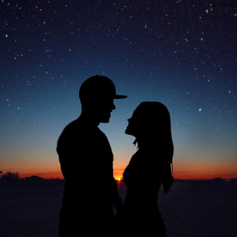 silhouette romantic couple standing face to face on field against star field
