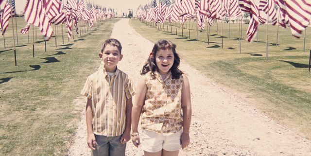 Caucasian brother and sister holding hands near American flags