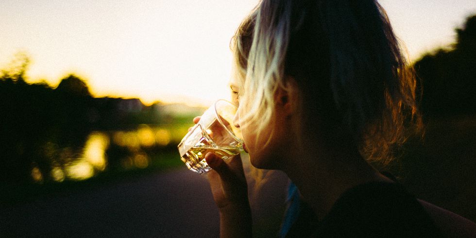 Close-Up Of Woman Drinking Whiskey Against Sky