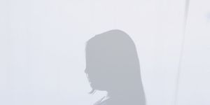 a transparent silhouette of a pregnant woman standing above a field of trees