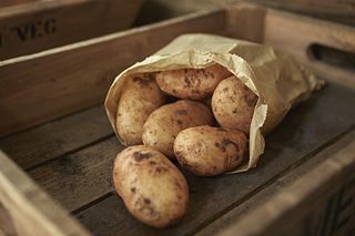 Still life close up rustic fresh, organic, healthy dirty potatoes in bag in wooden crate