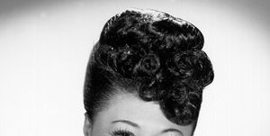 ella fitzgerald smiles at the camera, she wears a beaded short sleeve top with a necklace and stud earrings