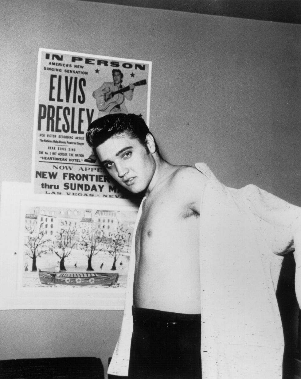 Rock and roll singer Elvis Presley in front of a concert poster with his shirt half on at the New Frontier Hotel on April 23, 1956 in Las Vegas, Nevada.
