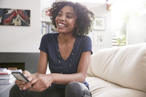 Smiling African American woman with cell phone on living room sofa