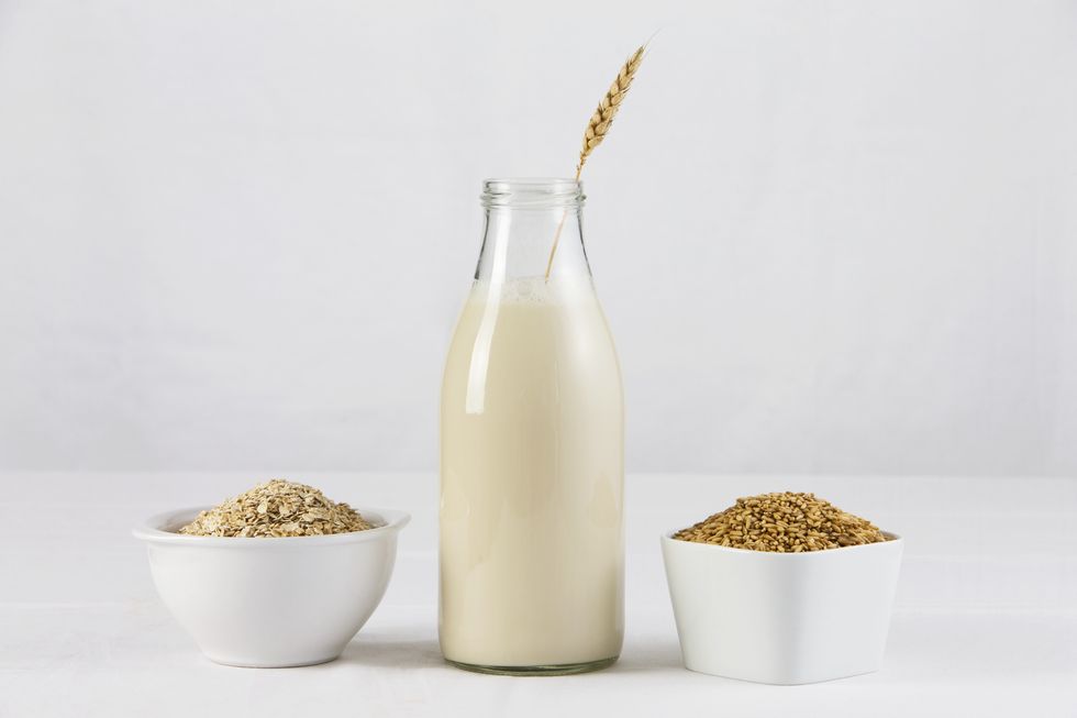 a bottle of oat milk with two dishes of oats and oatmeal