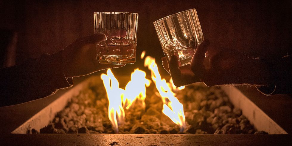 Cropped Hands Of Couple Toasting Scotch Whiskey Glasses By Bonfire
