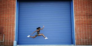 Mixed Race woman running and jumping near blue garage door