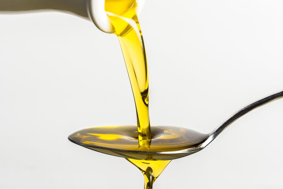 closeup of olive oil pouring on spoon from container against white background