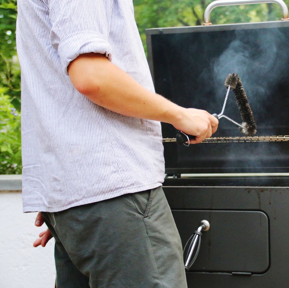 Midsection Of Man Cleaning Barbecue Grill With Wire Brush