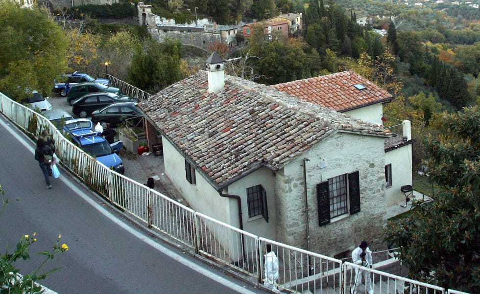 a house sits on the side of a cliff with other buildings, trees and cars in the background