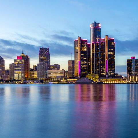 the skyline of detroit in the evening, with pink lights on many of the buildings for breast cancer awareness the skyline is reflecting off the detroit river