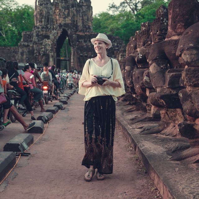 female tourist walks among statues at sunset near bayon temple, near angkor wat, siem reap, cambodia