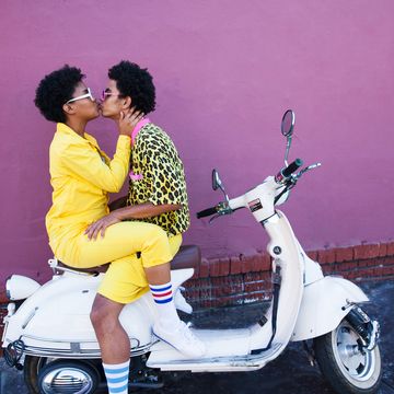 a young couple wearing yellow outfits sitting on a scooter kissing