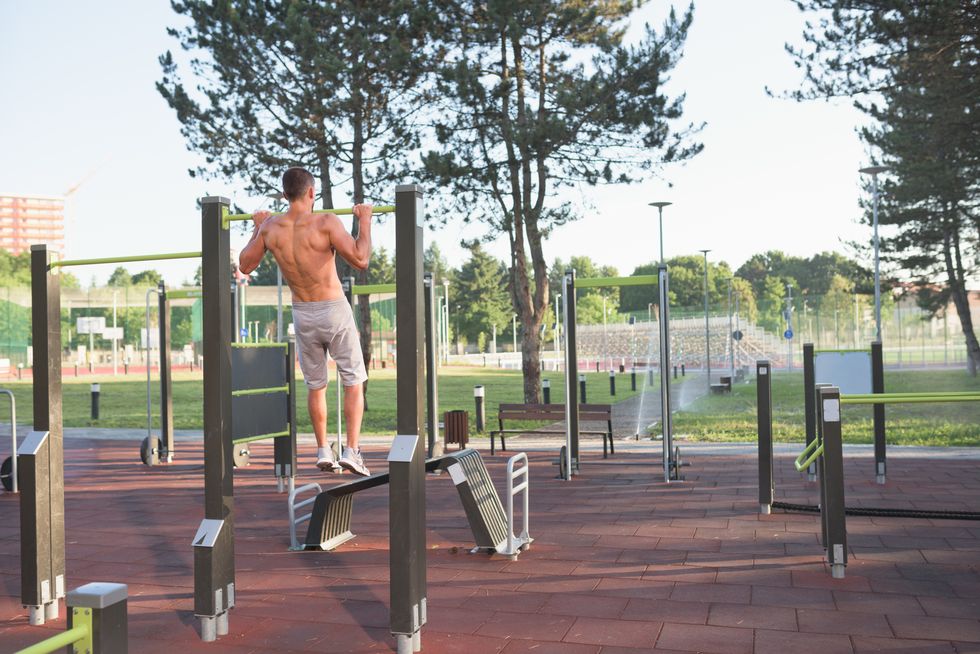 back view of male bodybuilder doing chin ups outdoor in the park